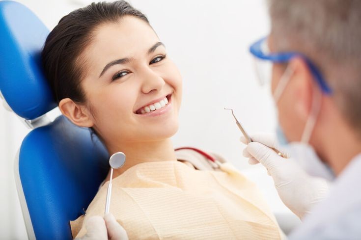 Woman in a dentist chair smiling in front of a dentist